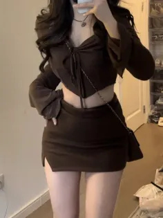 Woman in a dark brown crop top and mini skirt with a shoulder bag indoors