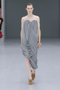 Model in a gray strapless draped dress on a runway