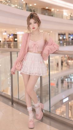 Woman in a pink cardigan and white lace skirt posing in a mall