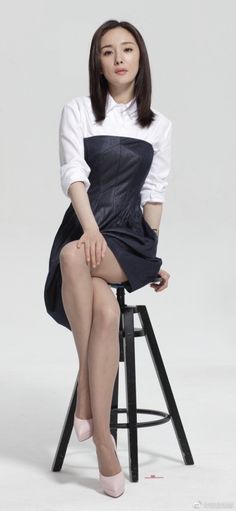Woman in a white shirt and denim dress sitting on a stool
