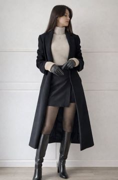 Woman in a black long coat, mini skirt, and knee-high boots indoors