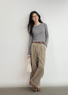 Woman with long black hair and glasses wearing a gray shirt and khaki pants