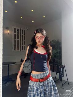 Woman with pigtails and red glasses wearing a crop top and plaid skirt indoors