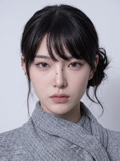 Woman with black hair in a messy bun and bangs wearing a gray top