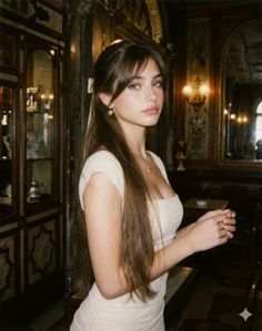 Woman with long brown hair in a light dress indoors with warm lighting