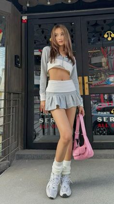Woman in a crop top and mini skirt with a pink bag and leg warmers outdoors