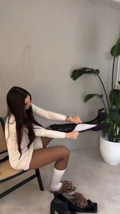 Woman in a white dress and black tights putting on knee-high boots indoors