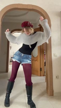 Person in a red beret, cropped sweater, denim shorts, and burgundy tights posing indoors