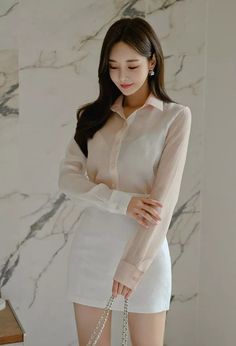 Woman in a white sheer shirt and white skirt holding a bag indoors