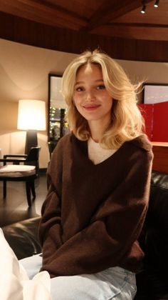 Young woman with blonde hair in a brown sweater smiling indoors