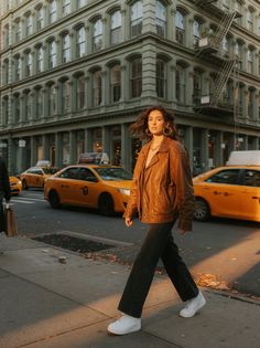 Woman in a brown leather jacket walking on a city street at golden hour