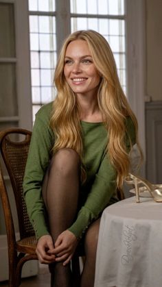 Woman with long blonde hair and a green sweater sitting indoors