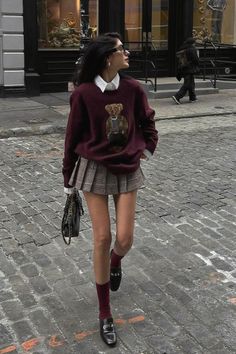 Woman in a plaid skirt and sweater walking on a cobblestone street