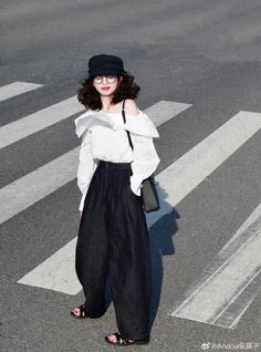 Woman with curly hair wearing a white blouse and wide-leg pants on a crosswalk
