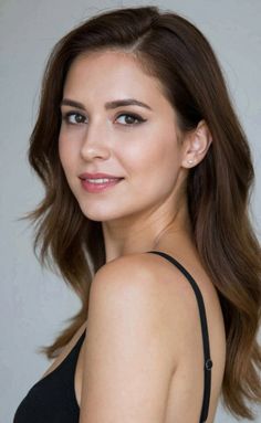 Woman with long brown hair wearing a black strap top, looking over her shoulder