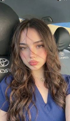 Woman with long wavy hair and a blue top in a car interior