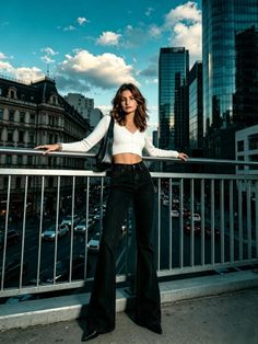 Woman in a white crop top and black flared jeans on a city bridge