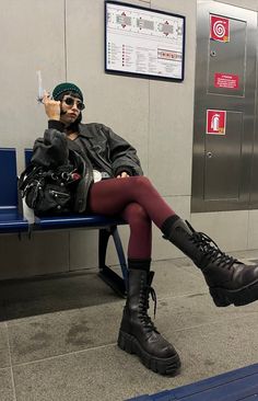 Person in a leather jacket and red tights sitting on a bench in a subway station