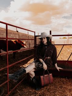 Woman in a cowboy hat and boots sitting on a fence at a farm