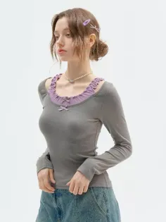 Woman in a gray long sleeve shirt with purple ruffle trim and a denim skirt
