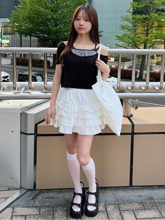Woman with long hair wearing a black top and white ruffled skirt outdoors