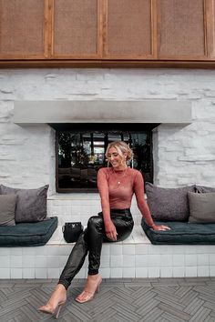 Woman in a sheer top and leather pants sitting on a tiled bench indoors