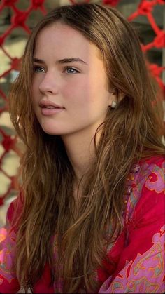 Young woman with long brown hair wearing a red patterned top