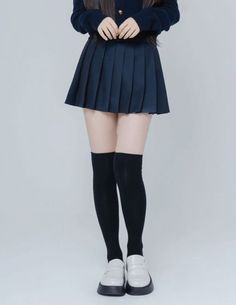 Person wearing a dark pleated skirt, knee-high socks, and white loafers
