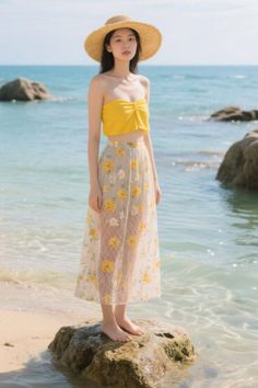 Woman in a straw hat and yellow top standing on a rock at the beach