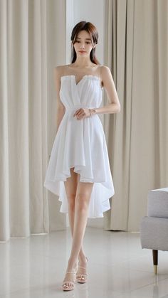 Woman in a white high-low dress with sheer neckline and high heels indoors