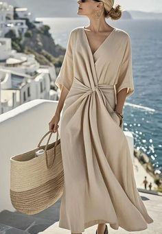 Woman in a beige maxi dress and sunglasses holding a straw bag in a coastal town