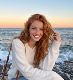 Woman with red hair and freckles smiling by the ocean at sunset