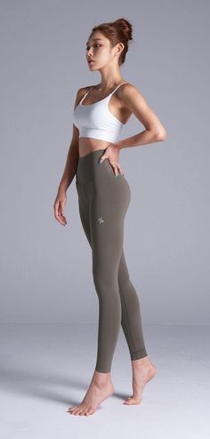 Woman in a white sports bra and olive leggings posing in a studio
