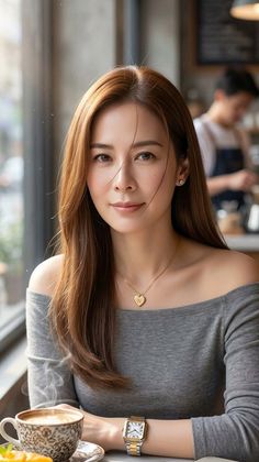 Woman with long brown hair wearing an off-shoulder top in a cafe