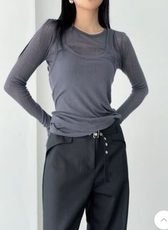 Woman with long black hair wearing a gray sheer top and black pants indoors