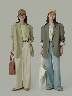 Two women in blazers, wide-leg pants, and baseball caps posing in a studio