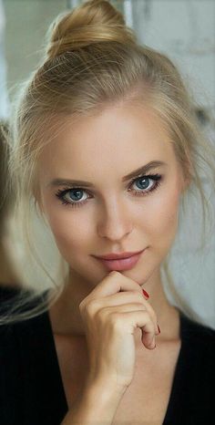 Blonde woman with blue eyes and an updo, resting her chin on her hand