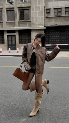 Woman in a brown leather jacket and black shorts posing on a street