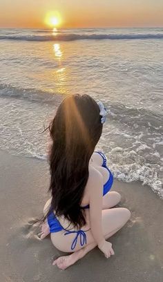 Woman in a blue bikini sitting on a beach at sunset