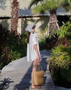 Woman in a white shirt and scarf holding a straw bag on a wooden path