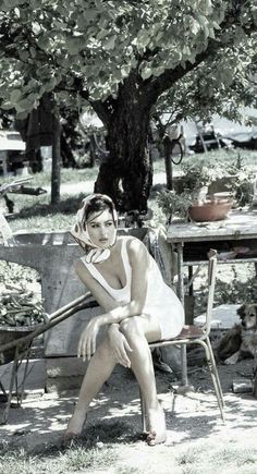 Woman in a white dress and head scarf sitting outdoors with a dog nearby