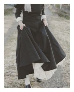 Person in a long black dress with white cuffs and ruffled underskirt walking outdoors