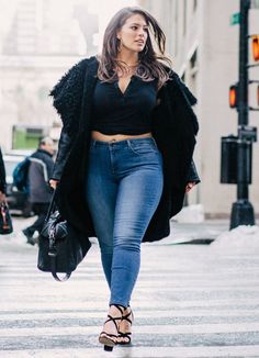 Woman in a black crop top and blue jeans walking on a street