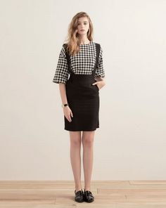 Woman in a houndstooth top and black dress standing indoors