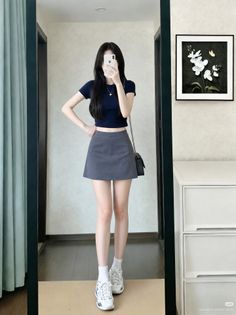 Woman in a crop top and mini skirt taking a mirror selfie indoors