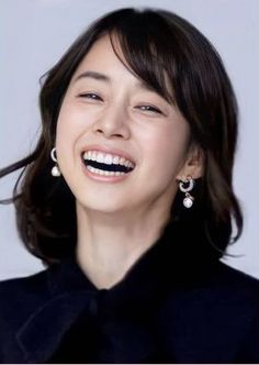 Woman with short dark hair and pearl earrings smiling brightly