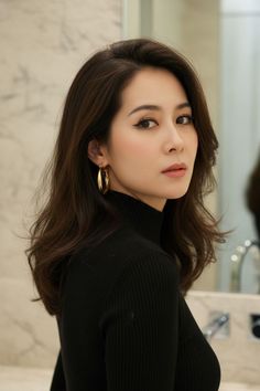 Woman with long dark hair wearing a black turtleneck and gold hoop earrings