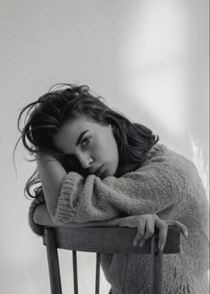 Woman with long hair in a fuzzy sweater, leaning on a chair in black and white