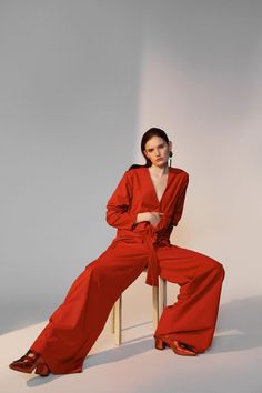 Woman in a red jumpsuit and earrings sitting on a stool in a studio