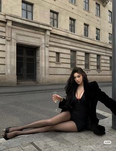 Woman in a black dress and tights sitting on a street with a glass of wine